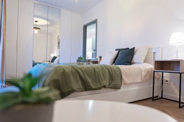 Konforlu, çift kişilik yataklı, yeşil yastıklı, güzel ve kapalı alanda minimalist bir yatak odası. Gardırobu olan modern bir ev ve otel odası. ve ayna. Şık mimari. Emlak.