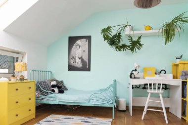 Odanın içi rahat, duvarında pastel rengi ve dekorunda sarı renk olan bir çocuk. Modern tasarımda yatak, koltuk ve halı olan tavan arasında bir oda. İskandinav konsepti.