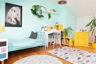 Odanın içi rahat, duvarında pastel rengi ve dekorunda sarı renk olan bir çocuk. Modern tasarımda yatak, koltuk ve halı olan tavan arasında bir oda. İskandinav konsepti.