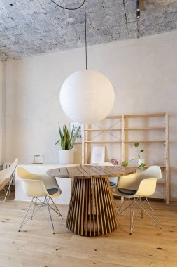 Modern ve rahat bir tasarım odası, ahşap yuvarlak masa, ahşap zemin ve lüks sandalye. Odunlu yeni bir daire. Dikey.