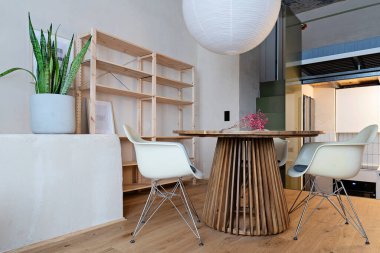 Modern bir mutfağın içinde yemek odası, tasarım koltuğu, ahşap zemin ve beton tavanda beyaz lamba olan yuvarlak bir masa. Oteldeki rahat oturma odası..