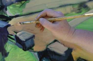 Resim fırçası ve resim tutan bir elin fotoğrafı.