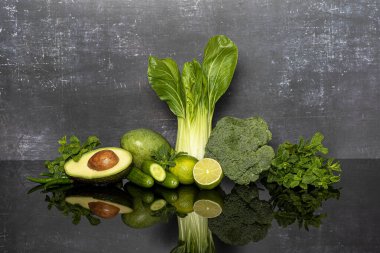 Yeşil sebzeler, brokoli, limon, nane, salatalık, avokado, acı biber, pak choi, gri arkaplanda mango.
