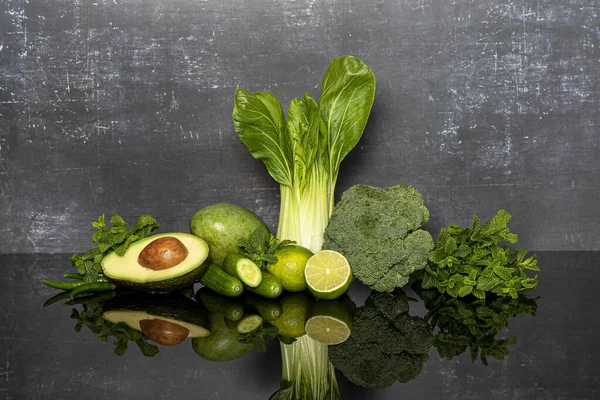 Yeşil sebzeler, brokoli, limon, nane, salatalık, avokado, acı biber, pak choi, gri arkaplanda mango.