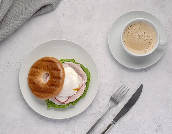 Food photography of bagel with poached egg, radish, bacon, ham, coffee, cappuccino, latte; Romaine lettuce; sandwich; morning; sliced; breakfast; brunch