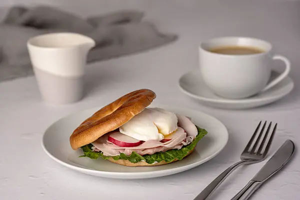 Food photography of bagel with poached egg, radish, bacon, ham, coffee, cappuccino, latte; Romaine lettuce; sandwich; morning; sliced; breakfast; brunch