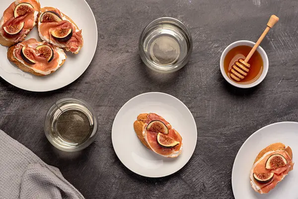 Bruschetta 'nın yemek fotoğrafları, yumuşak peynirli tost, jambon ve incir, bal, beyaz şarap, kahvaltı, arka plan.