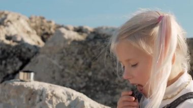 Little girl biting chocolate. Blonde girl squeezes his eyes shut with pleasure on sea background. Close-up.