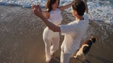 Güzel kız adamla dans ediyor. Beyaz elbiseli genç adam ve kadın gün doğumunda çakıl taşı plajında yürüyorlar. Yüksek açı görünümü