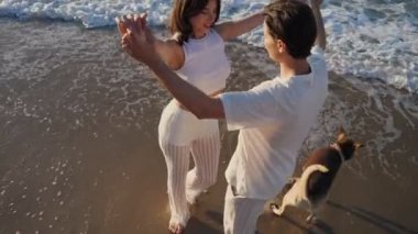 Güzel kız adamla dans ediyor. Beyaz elbiseli genç adam ve kadın gün doğumunda çakıl taşı plajında yürüyorlar. Yüksek açı görünümü