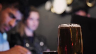 Üç çok ırklı insan, bar restoranının masasında dizüstü bilgisayarlı bir projede birlikte çalışıyor. Ön planda bir bardak bira..