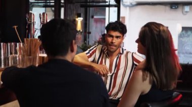 Bira barında kutlama yapan üç çok ırklı arkadaş. Genç İspanyol adam arkadaşlarıyla konuşuyor. Orta boy.