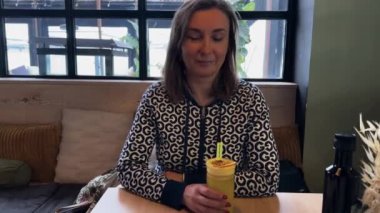 Güzel, beyaz bir kadın kafeteryada camdan portakal kokteyli içiyor. Orta boy.