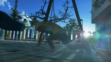 Beyaz çocuk parkta salıncakta sallanıyor. Sarı kapüşonlu yelek giyen şirin bir kız park alanında hızlı dönüyor. Düşük açı görünümü