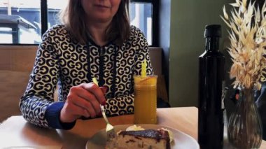 Kafeteryada güzel beyaz bir kadın peynirli keki ısırıyor. Orta boy.