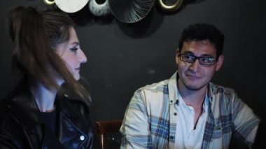 Bilgisayarlı bir projede birlikte çalışan üç genç insan bar restoranındaki masada oturup yazma, konuşma ve araştırma konusunda fikir alışverişinde bulunuyorlar. Orta boy.