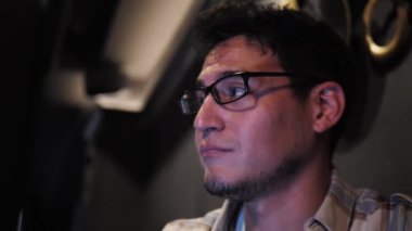 Gözlüklü Latin Amerikalı iş arkadaşlarıyla konuşuyor. Üç çok ırklı insan, bar restoranının masasında oturmuş, dizüstü bilgisayarla beyin fırtınası yaparak ve araştırma yaparak bir proje üzerinde çalışıyor. Yakın çekim.