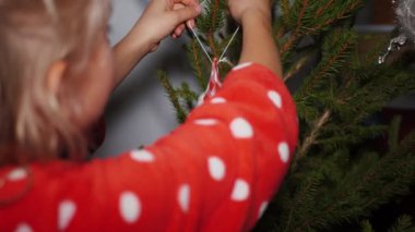 Kırmızı pijamalı genç kız Noel ağacını el yapımı melek oyuncağıyla süslüyor.