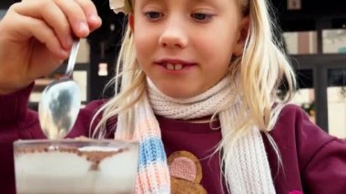 Boynunda eşarbı olan, açık verandada kakao sütü ve çikolatalı çöreğin değerini bilen genç bir kız. Çocuk kaşıkla milkshake karıştırıyor. Yakın plan.