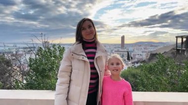 Gülümseyen anne ve kız turistlerin portresi güzel bir günbatımının keyfini çıkarıyor. Arka planda kıyı kenti.