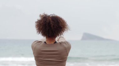 Yoga eğitmeni derin nefes alma alıştırması yapıyor, meditasyon pozisyonunda duruyor, ellerini kaldırıyor, dingin okyanus manzaralı bir ortamda sakinleşme dönemi geçiriyor. Orta boy yakın çekim