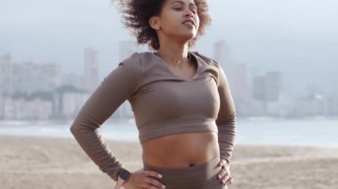 Fit bir kadın okyanus kıyısında dinamik esneme hareketleri yapıyor. Kaslı vücudu, sabahın erken saatlerinde yoğun plaj temelli fitness antrenmanına hazırlıyor.