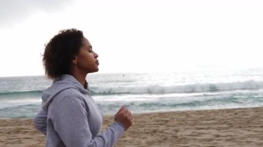 Fitness İspanyol kadın arkada fren yapan deniz dalgalarıyla kumsalda ağır çekimde koşuyor, sağlıklı bir yaşam tarzının tadını çıkarıyor. Orta boy.