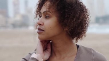 Genç İspanyol kadının yakın çekimi dalgalı saçlarını kumlu sahilde dalgalandırıyor güneşli yaz günlerinde manzaralı okyanus ve dağ manzarasına bakıyor.