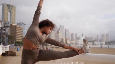 İspanyol fitness modeli, güneşli şehir terasında bacaklarını esnetiyor. Benidorm şehir manzarasına karşı denge ve güç gösterisi sergiliyor.