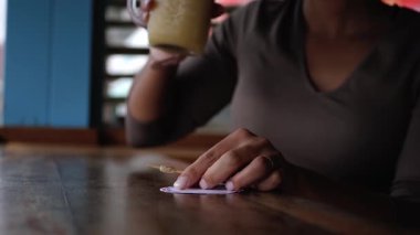 Rahat genç Afrikalı Amerikalı kadın sahildeki barda otururken ferahlatıcı bir içecek yudumluyor. Cam ve kadın elleri ön planda..