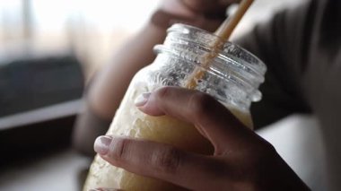 Sarı-yeşil smoothie ile bardağı tutan kadın ellerinin yakın çekimi. Genç Afrikalı Amerikalı kadın sahildeki barda otururken ferahlatıcı bir içki yudumluyor..