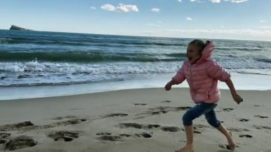 Kumlu sahilde kış denizinden koşan ve düşen güzel bir kız. Yavaş çekim
