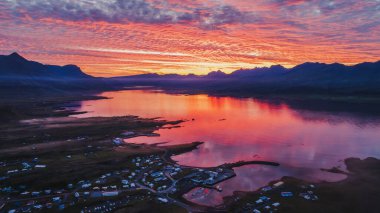 Küçük bir İzlanda kasabası dağlarla çevrili sakin bir fiyordun yanında oturur. Günbatımı gökyüzü suya yansıyarak, sakin ve canlı bir sahne yaratıyor..