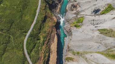 Turkuaz nehri, bir tarafı yemyeşil, diğer tarafı kayalık bir araziyle çevrili küçük bir şelale ile engebeli bir kanyondan akar..