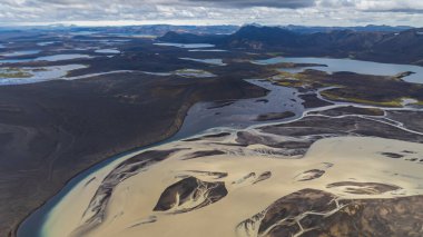Örülmüş nehirler ve ışık çökeltileri İzlanda 'nın dağlık bölgelerindeki uzak dağlar ve dağınık göller tarafından çerçevelenmiş karanlık volkanik arazide akıyor..