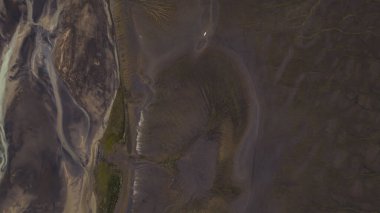 Sönük tonlar, kıvrımlı alüvyonlu nehirler ve geniş bir çevreyi vurgulayan küçük beyaz bir nesnenin yer aldığı İzlanda hava görüntüsü..