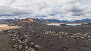 Renkli rhyolite dağları, karanlık lav alanları, dingin bir göl ve bulutlu gökyüzü ile İzlanda 'nın Landmannalaugar bölgesinin dramatik hava manzarası..