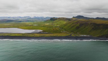 İzlanda 'nın güney sahilinin dramatik hava manzarası. Siyah kumsal, yeşil tarlalar, engebeli tepeler, küçük bir yerleşim yeri ve sakin iç sular..