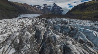 İzlanda 'da buzul manzarası, yarık buzlar, çökelti çizgileri, karlı dağlar, yeşil yamaçlar ve parçalı bulutlu bir gökyüzü..