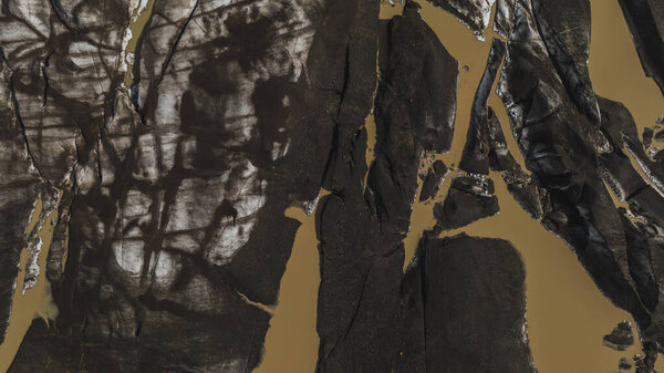 Тёмные, зазубренные скальные образования с грязными коричневыми ледниковыми каналами создают абстрактные узоры, демонстрирующие пересечённую и впечатляющую местность Исландии..