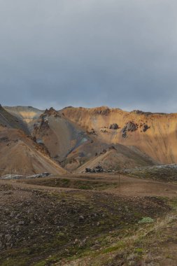 Topraksı tonları, yeşil yosunları olan renkli ryolite dağları ve Landmannalaugar, İzlanda 'da bulutlu bir gökyüzünün altında soluk bir iz..