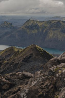 Keskin sırtları, turkuaz gölü ve dik yosunları olan engebeli volkanik arazi İzlanda 'nın dramatik jeolojisinde bulutlu bir gökyüzünün altındaki uçurumları kapladı..