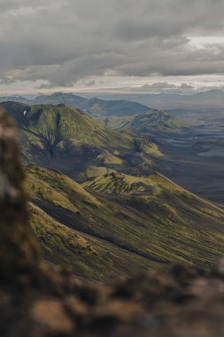 İzlanda 'da engebeli bir volkanik arazi yosun kaplı tepeler, karanlık toprak ve vadileri dramatik bulut gölgeleriyle kaplı bulutlu bir gökyüzünün altında barındırır..