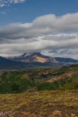 Yosun kaplı engebeli arazi, volkanik kaya ve kar parçalarından oluşan bir dağ silsilesi ve doğu İzlanda 'nın manzarasında bulutlu bir gökyüzü..