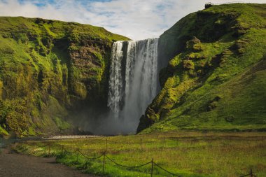 Güney İzlanda 'daki Skogafoss şelalesi 60 metre boyunca yeşil kayalıklarla çevrili. İp ve çimenlik alan sisli çağlayanı gösteriyor..