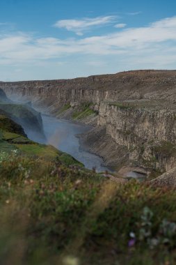 Sarmal bir nehri olan İzlanda 'da sarp bir kanyon, soluk bir gökkuşağı oluşturan sis, yeşil yosun, kır çiçekleri, kayalık uçurumlar ve açık mavi bir gökyüzü..