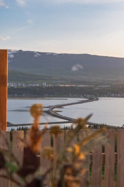 İzlanda 'da sakin su üzerinde kıvrımlı bir yolu olan bir sahil manzarası, karlı dağların eteğinde yumuşak bir gökyüzünün altındaki bir kasabaya götürüyor..