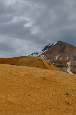 Landmannalaugar bölgesinde bulutlu bir gökyüzü altında renkli bir rhyolite dağının yer aldığı engebeli İzlanda manzarası.