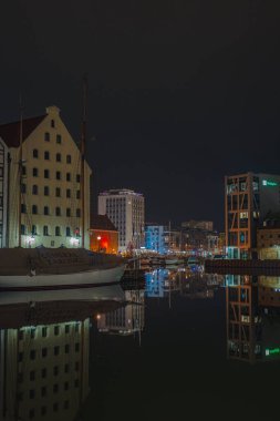 Polonya 'nın Gdansk kentinde sakin bir nehir tarihi ve modern binaların ön cephelerini yansıtıyor. Beyaz bir yelkenli, karanlık bir gökyüzünün altına yanaştı..
