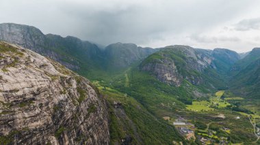 Dik uçurumlar, yemyeşil vadiler, dağınık binalar, tarım arazileri ve bulutlu bir gökyüzünün altındaki sisli dağların bulunduğu Lysebotn, Norveç 'in dramatik hava manzarası..